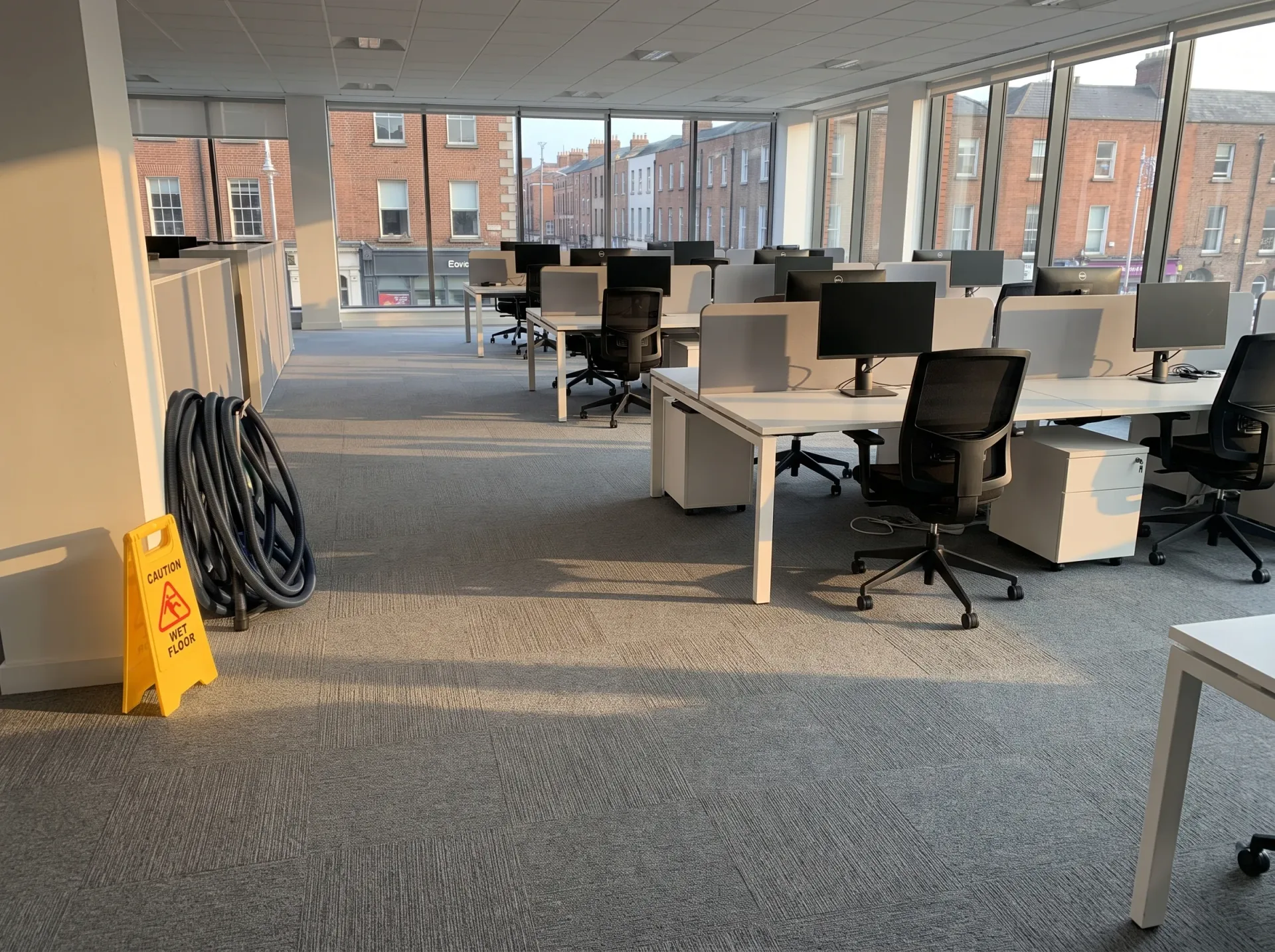 Office carpet flooring with commercial cleaning hose and caution sign in modern professional workspace