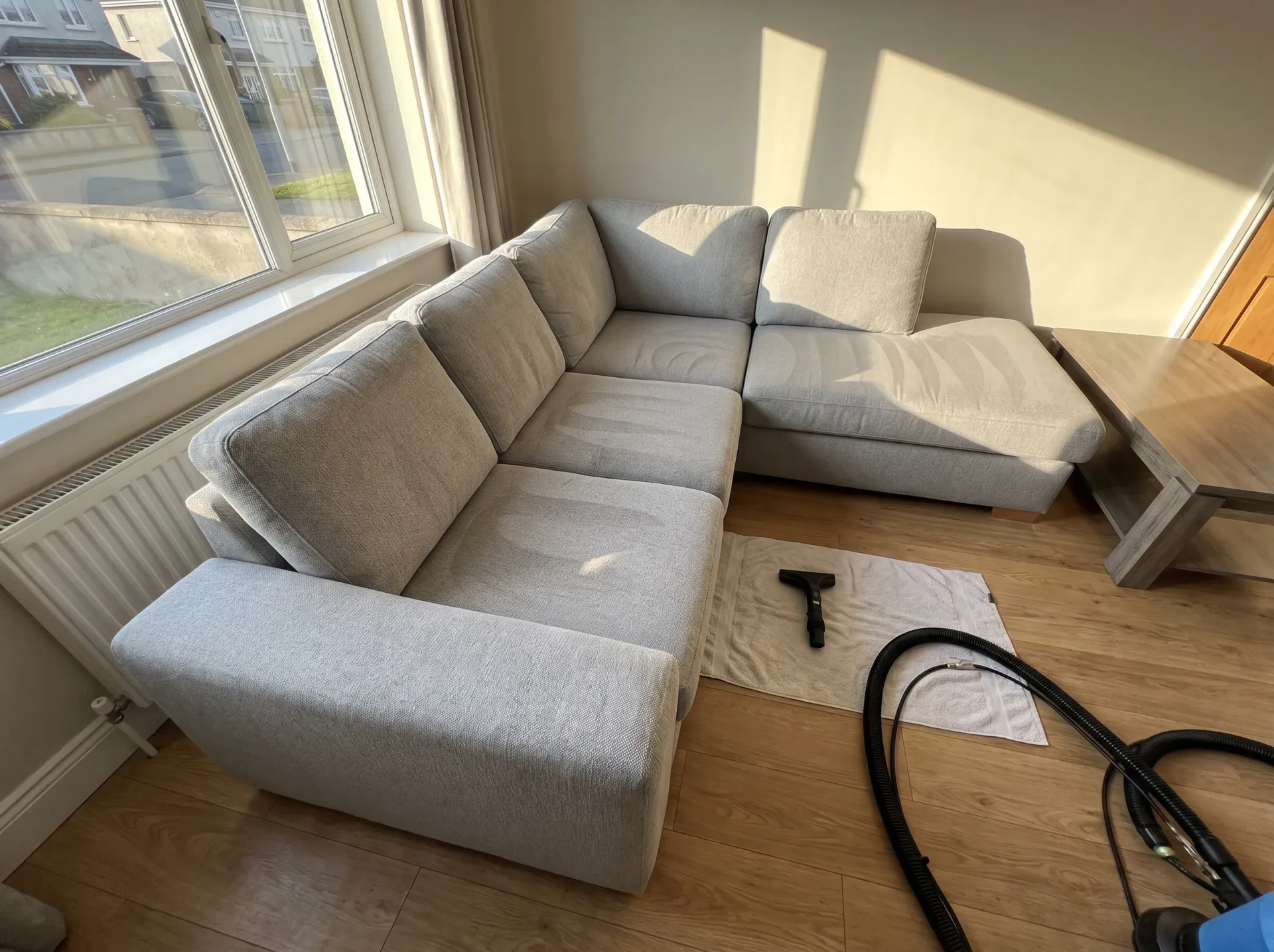 Gray corner sofa being professionally cleaned with hot water extraction equipment during upholstery cleaning service